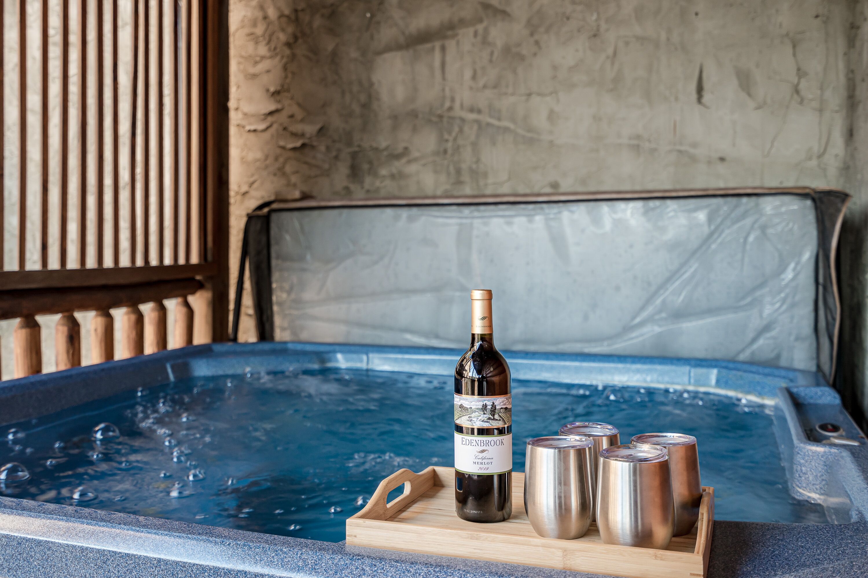 Eine Sitzecke mit Whirlpool, einer Flasche Edenbrook Wein und drei Edelstahlbechern auf einer Holztablett.