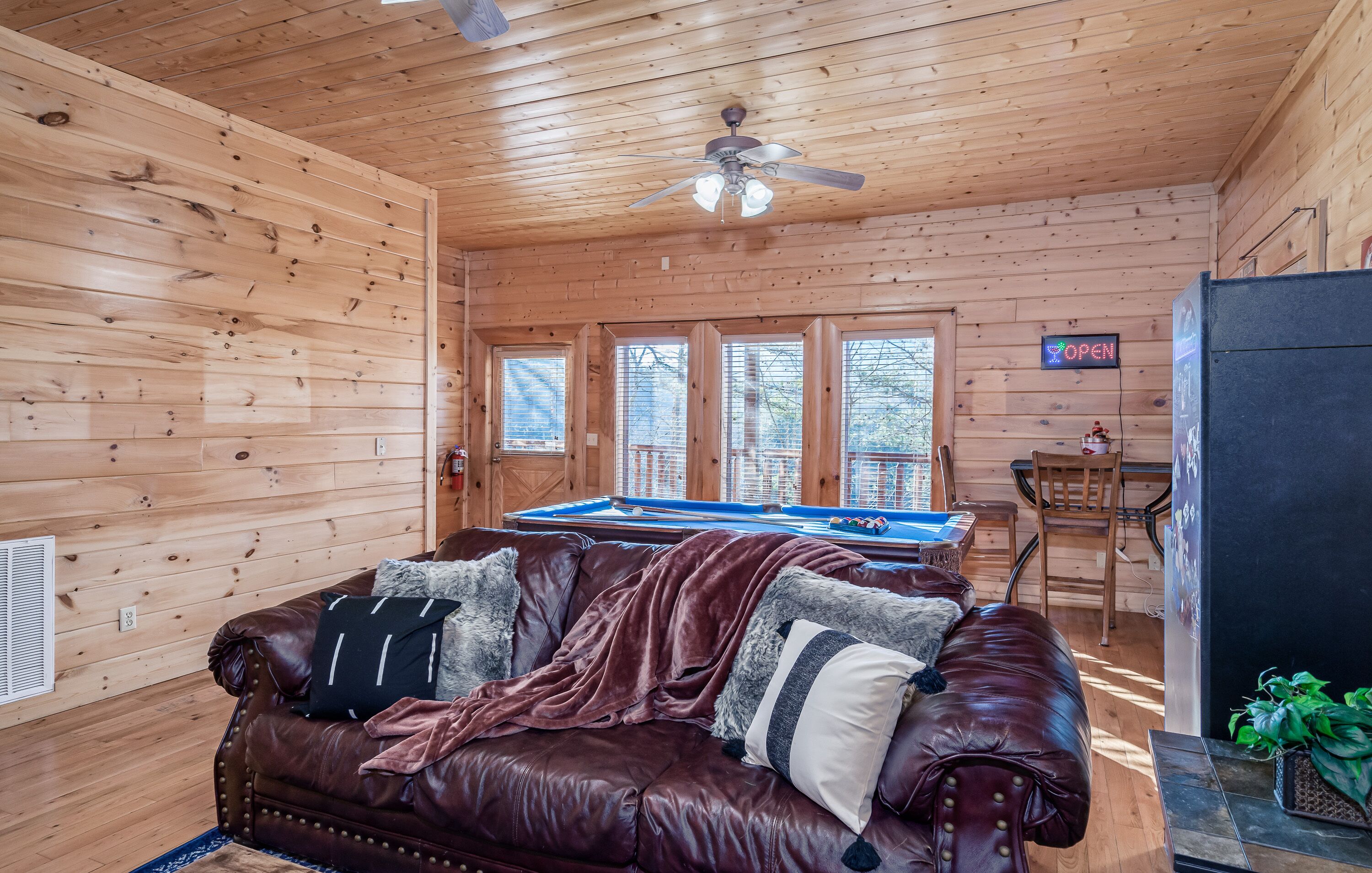 Ein Holzblockhaus-Innenraum mit Billardtisch, braunem Ledersofa und Deckenventilator.