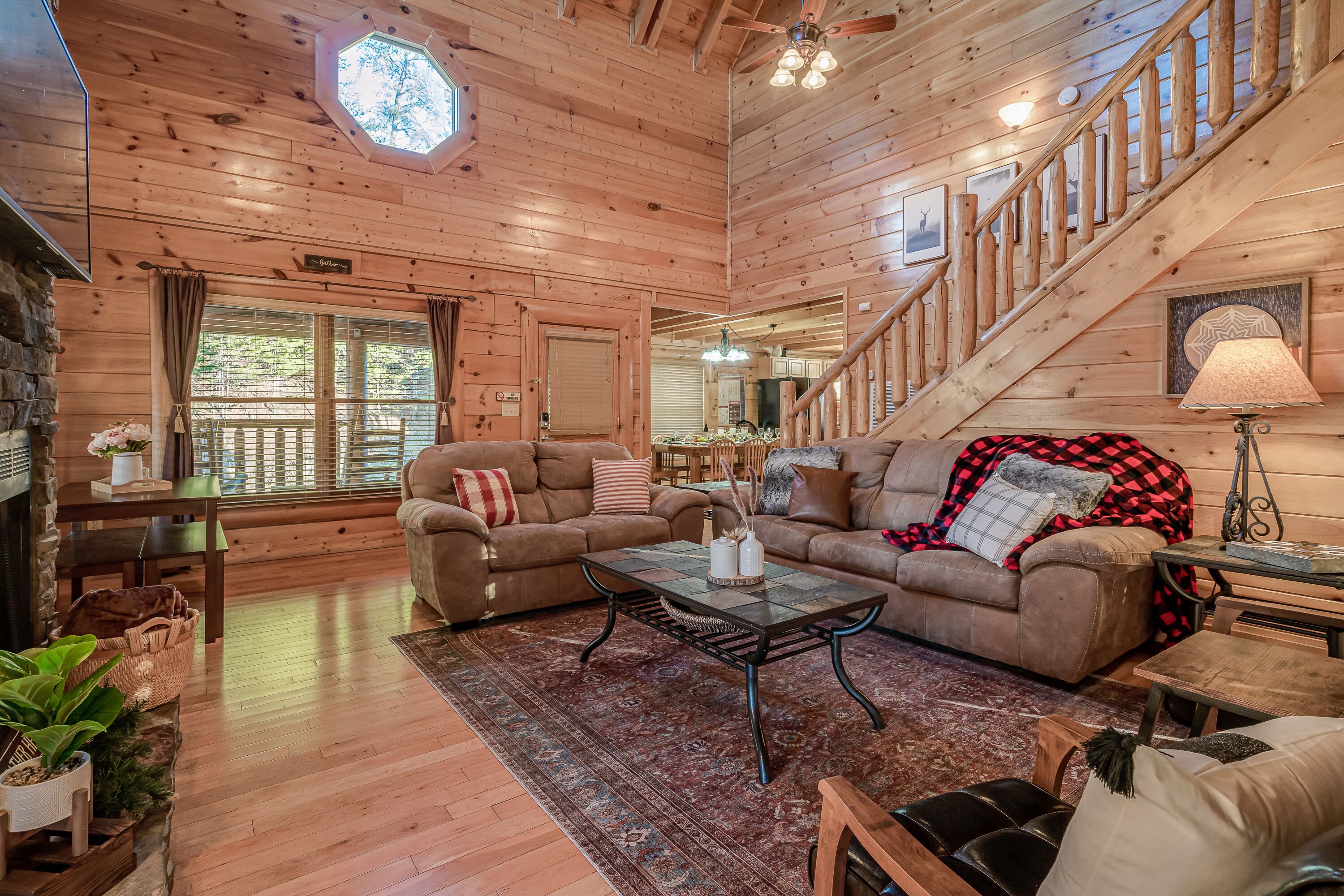 A cozy log cabin interior with a living room, dining area, and a staircase leading to a loft.
