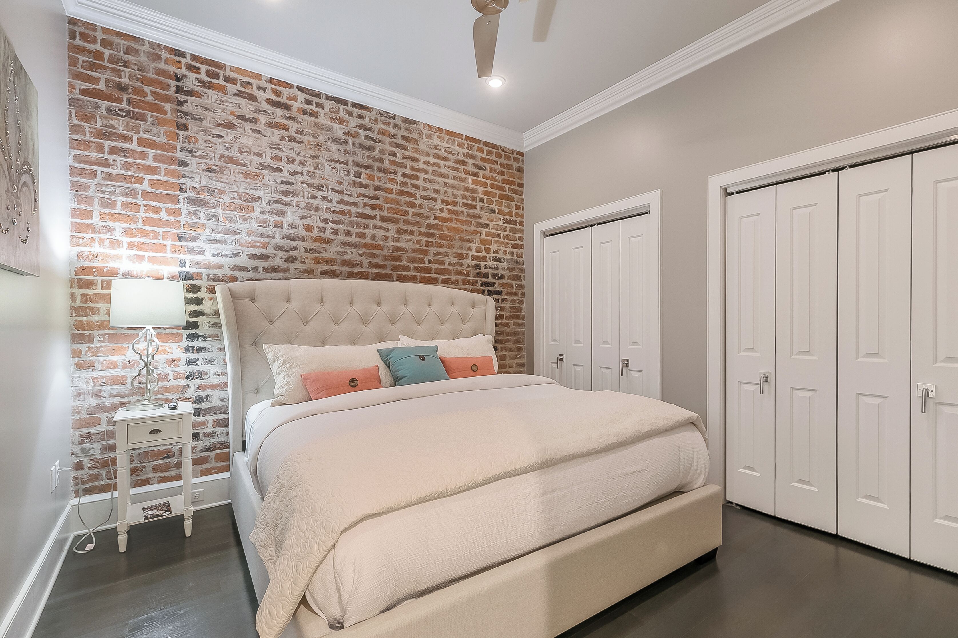 Une chambre avec un mur d’accent en briques, une tête de lit capitonnée, une table de chevet et une armoire.