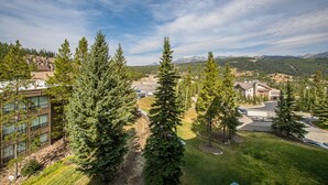 A residential area with modern buildings, a parking lot, and a mountainous backdrop. - Ski-In/Out Condo | Lone Peak Views & Community Pool/Hot Tub (Big Sky)