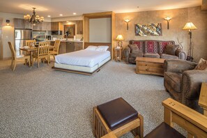 Una habitación de hotel con cama, sofá, mesa de comedor con sillas, zona de cocina y sala de estar con sofá y lámpara.