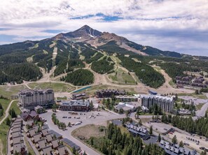 A mountain resort with multiple buildings, a ski lift, and a parking area. - Ski-In/Out Condo | Lone Peak Views & Community Pool/Hot Tub (Big Sky)