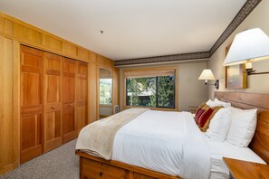 Quarto com cama grande, guarda-roupa de madeira, janela com vista e mesa de cabeceira com abajur.