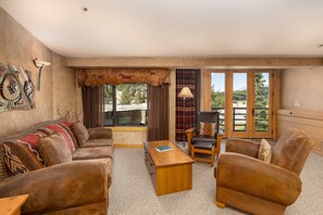 A living room with a sofa, armchairs, a coffee table, and a view of a mountain through large windows. - Ski-In/Out Condo | Lone Peak Views & Community Pool/Hot Tub (Big Sky)