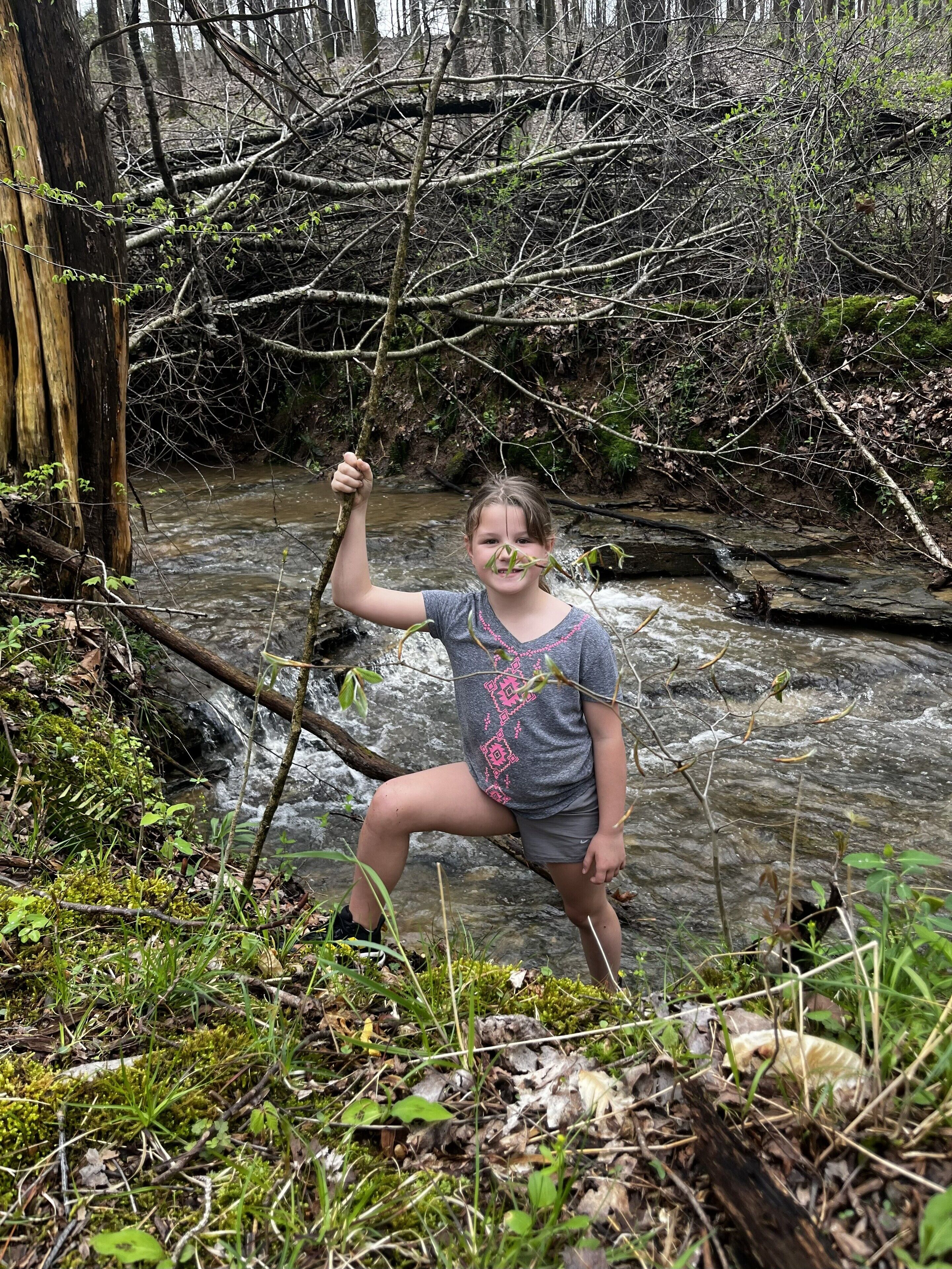 Una persona sentada sobre un tronco junto a un arroyo en un bosque.
