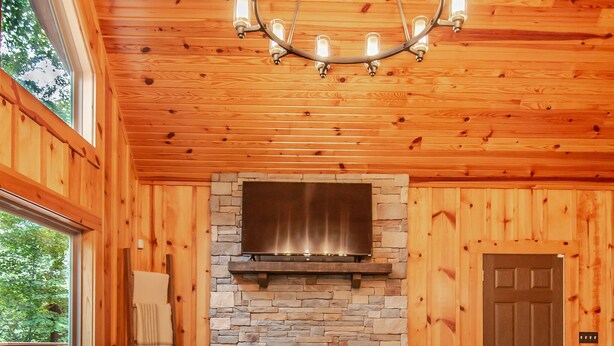 Interior acogedor de una cabaña con chimenea de piedra, sofá de cuero y candelabro.