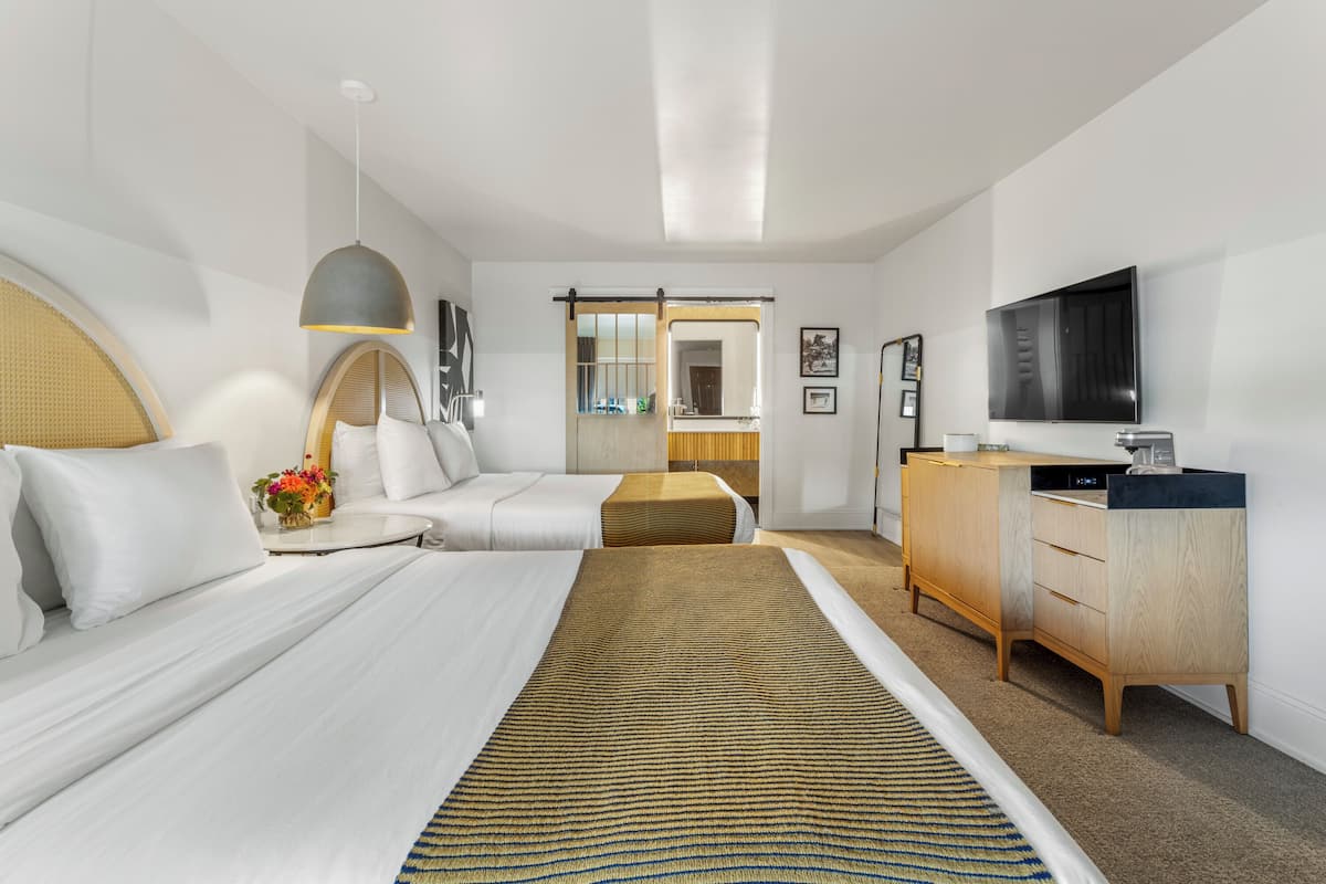 A hotel room with two beds, a large mirror, a television, and a wooden cabinet.