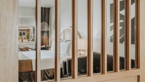 Una habitación de hotel con un ventanal grande, una cama, una mesita de noche y una lámpara.