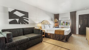 Una habitación de hotel moderna con una cama grande, un sofá, una mesita de noche, una lámpara y un cuadro abstracto de gran tamaño en la pared.