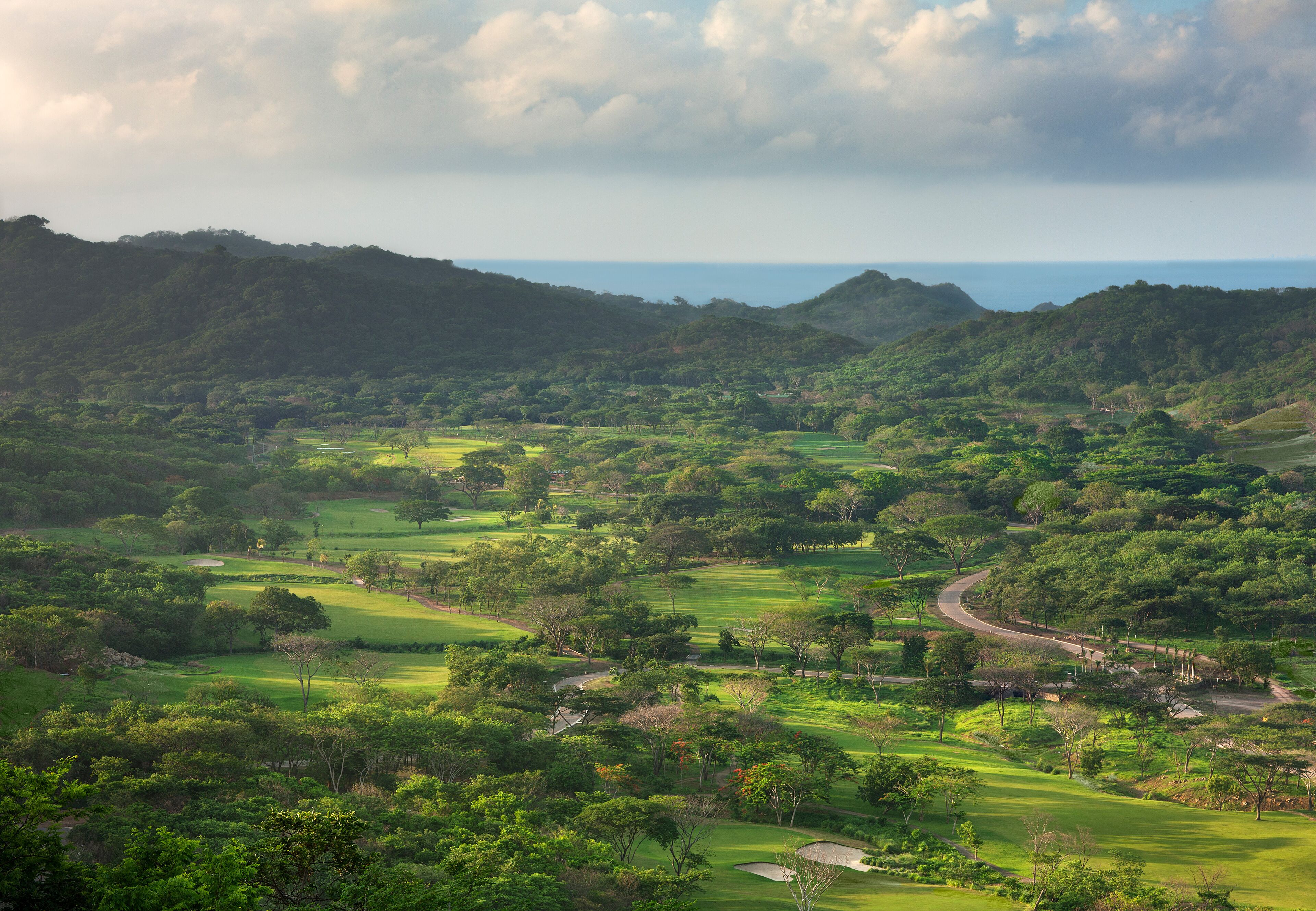 A golf course with multiple holes, surrounded by lush greenery and hills.
