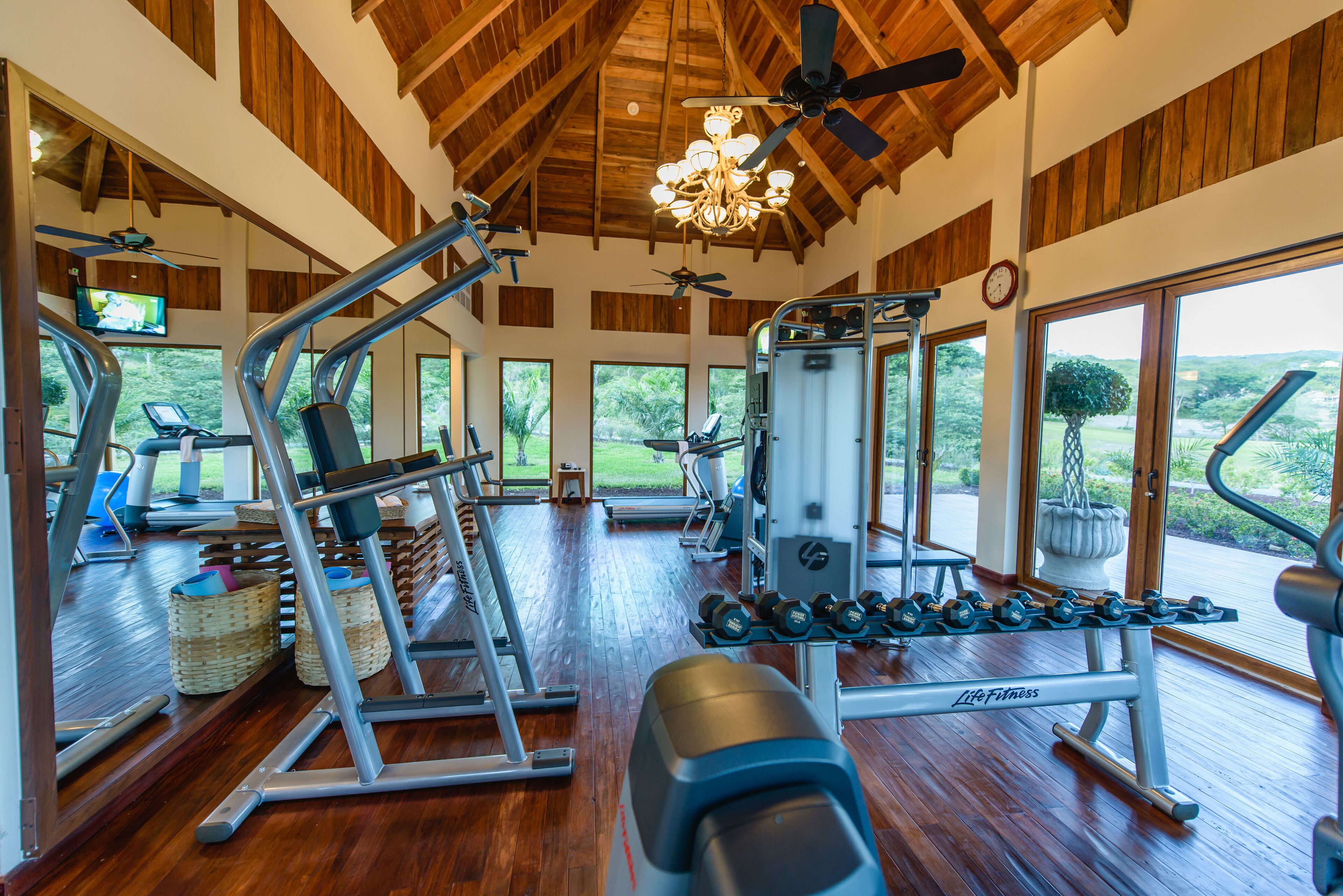 A spacious gym with various exercise equipment, large windows, and a wooden ceiling.