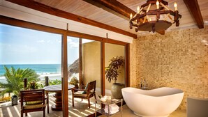 Un baño moderno con una bañera independiente, techo de madera y un amplio ventanal con vistas a la playa.