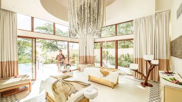 A spacious room with a large window, a hanging chandelier, and a massage table.