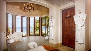 Una habitación amplia con una cama grande, una sala de estar con vista al océano y una puerta de madera.