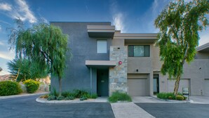 Une maison moderne à deux étages, dotée d’une façade en pierre, d’un garage et d’un jardin bien entretenu à l’avant, où diverses plantes sont cultivées.