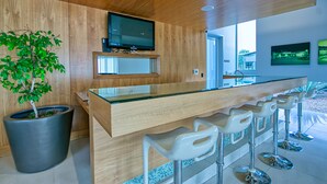 Une cuisine moderne avec des meubles en bois, un grand îlot central doté de tabourets, un téléviseur à écran plat et une plante en pot.