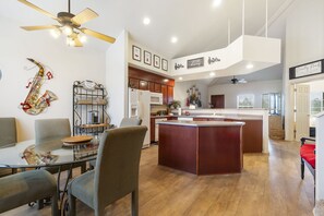 Een moderne keuken met een centraal eiland, houten keukenkastjes en een eethoek met een glazen tafel en stoelen.