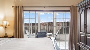 A hotel room with a large bed, a desk with a chair, a lamp, and a view of a building through large windows. - Family Getaway • Spacious 3BR Condo • Resort Amenities + Perks (Branson)