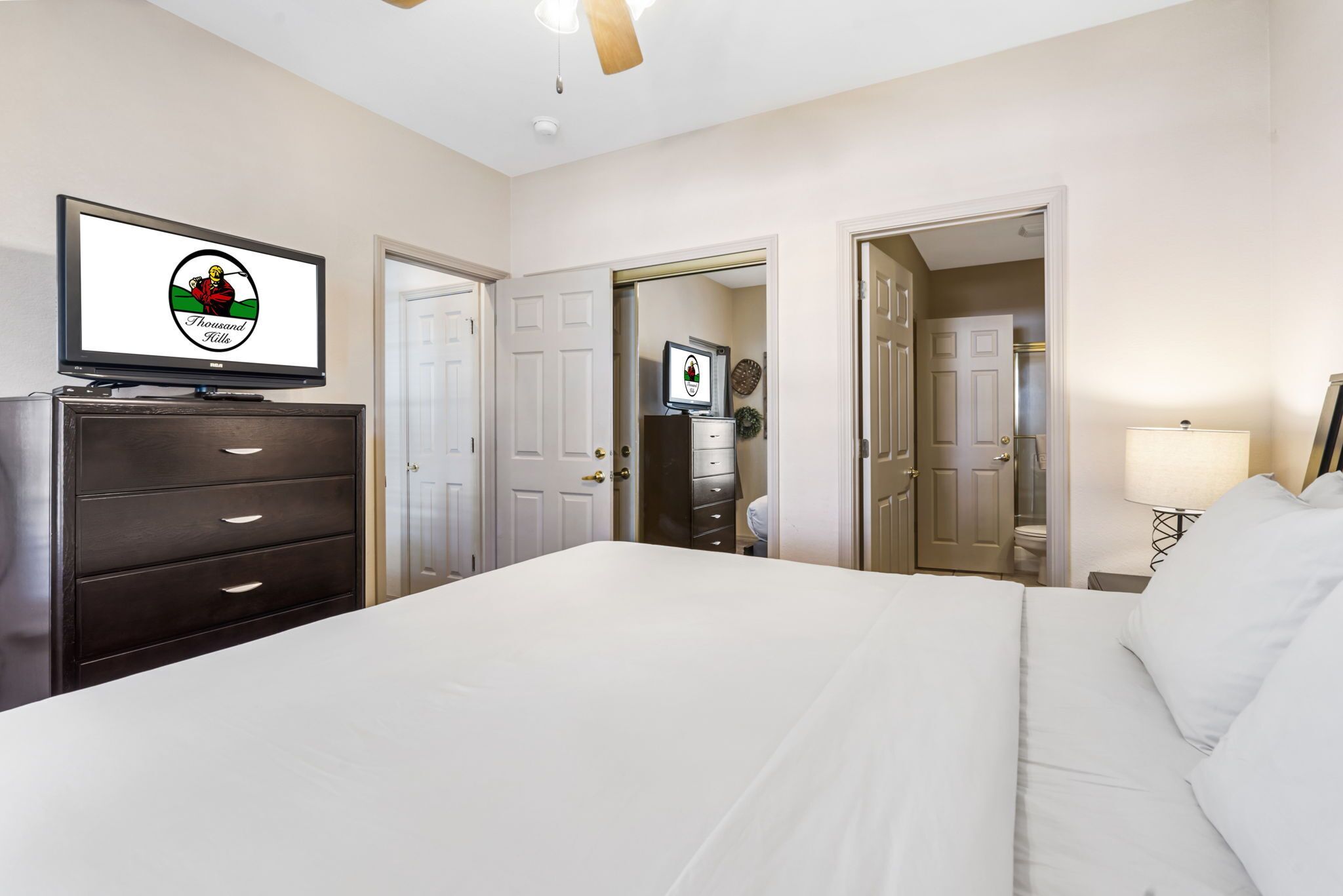 A hotel room with a bed, a dresser, a television displaying a logo, and a door leading to a bathroom.