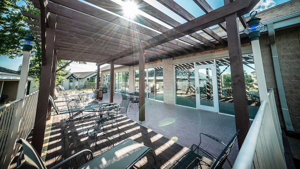 Um pátio externo com pérgola de madeira, mesas e cadeiras.
