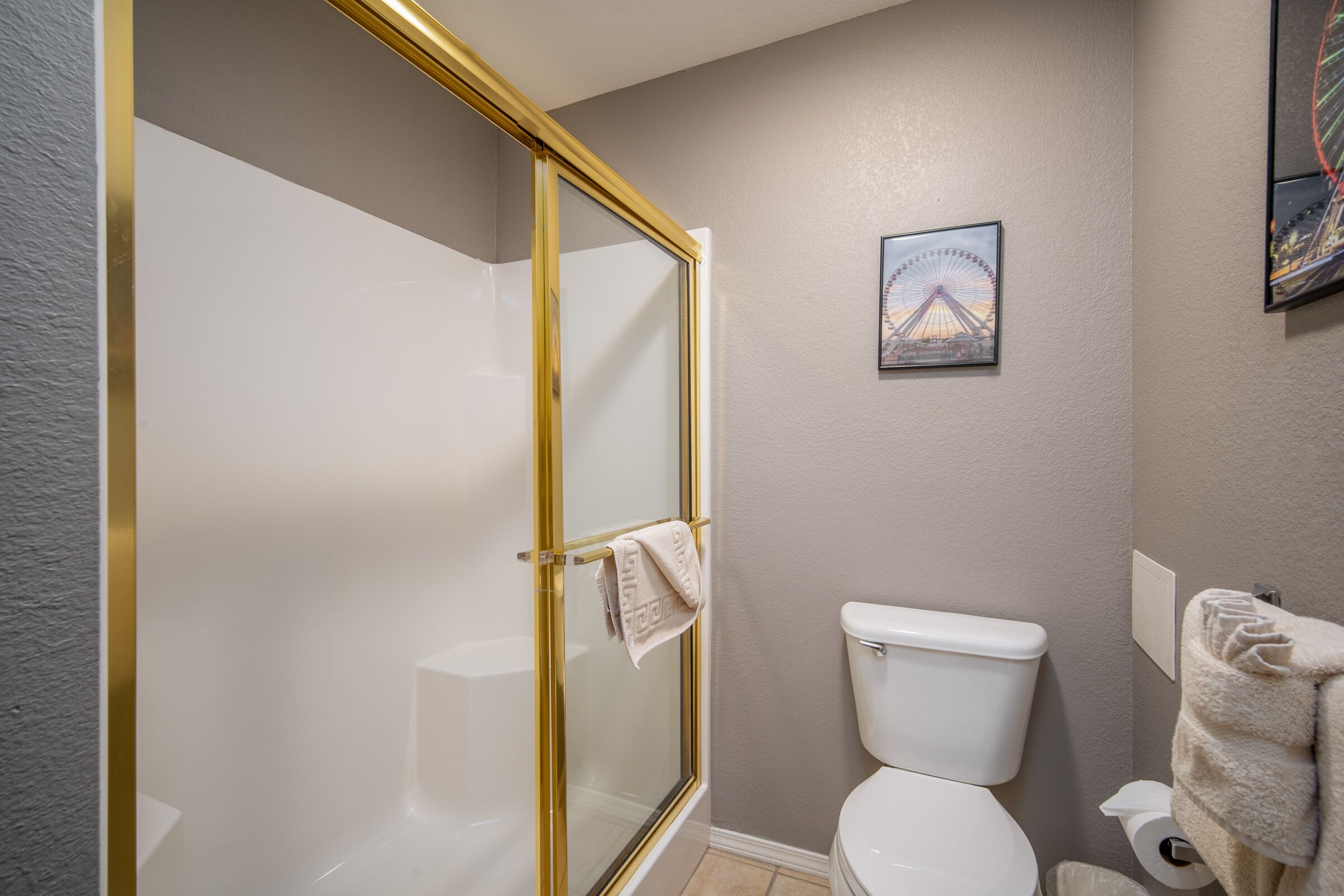 A bathroom with a glass-enclosed shower, a toilet, and a framed picture on the wall.
