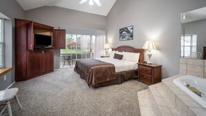 Een slaapkamer met een bed, televisie, bureau, stoel, raam en plafondventilator, plus een badkamer met bad.