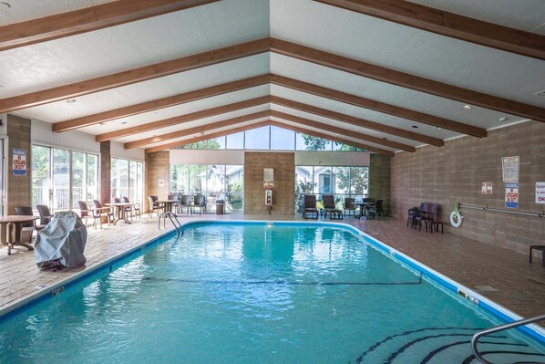 An indoor swimming pool with wooden beams, poolside chairs, and tables.