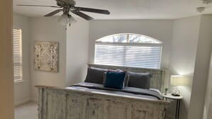 A bedroom with a rustic bed, a ceiling fan, a window with blinds, a wall-mounted lamp, and a decorative piece. - Amazing, Contemporary, Beautiful, Peaceful, and Perfectly Located Property (San Antonio)