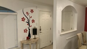 A hallway with a white door, a small table with a vase and a sign, and a chair with a striped cushion. - Amazing, Contemporary, Beautiful, Peaceful, and Perfectly Located Property (San Antonio)