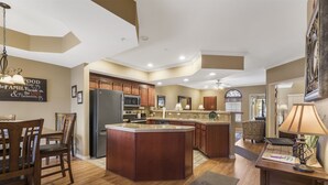 A kitchen with a central island, wooden cabinets, a refrigerator, and a dining area with chairs. - Family-Friendly Branson Stay • 2BR/2BA Condo Sleeps 6 • Sunroom + Guest Perks (Branson)