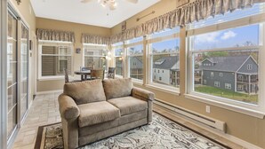 A spacious living room with a beige sofa, large windows, a ceiling fan, and a view of neighboring houses. - Family-Friendly Branson Stay • 2BR/2BA Condo Sleeps 6 • Sunroom + Guest Perks (Branson)