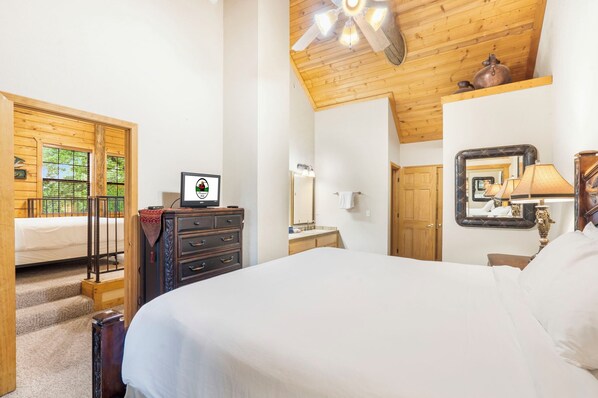 A bedroom with a wooden ceiling, a bed, a dresser, a mirror, and a window with a view of greenery. - Spacious Country Cabin (2BR+Loft) in Branson Theatre District (Branson)