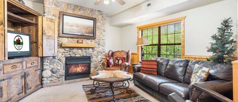 A cozy living room with a stone fireplace, leather sofa, and a Christmas tree.