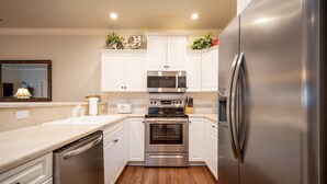 Una cocina compacta con armarios blancos, electrodomésticos de acero inoxidable y piso de madera.
