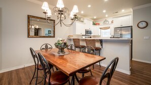 Un comedor con una mesa y sillas de madera, una araña y una cocina con armarios y electrodomésticos blancos.