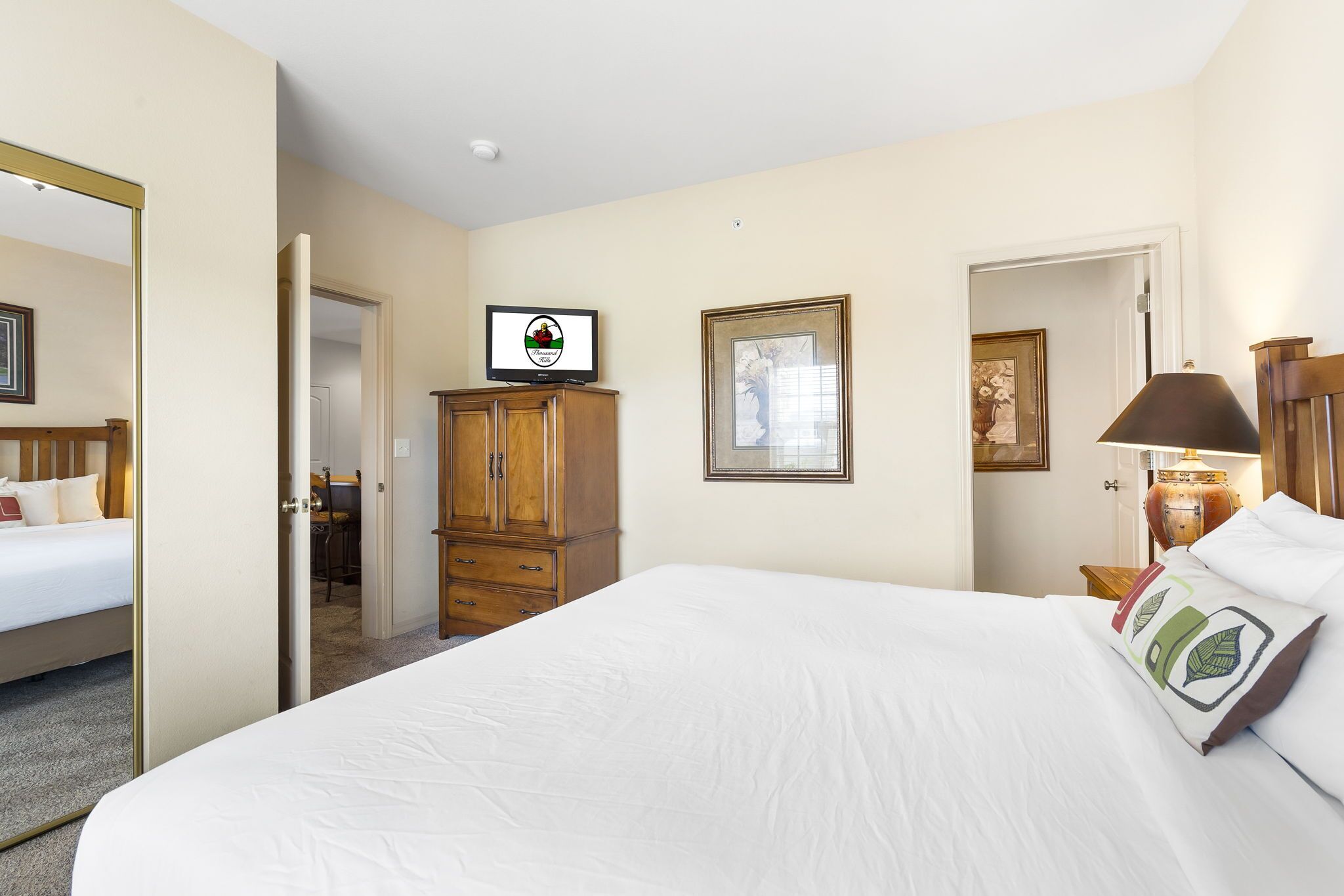 Ein Hotelzimmer mit einem großen Bett, einem Holzschrank, einem Fernseher und einem gerahmten Bild an der Wand.