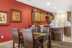 A dining area with a wooden table and chairs, a kitchen with wooden cabinets, and artwork on the walls.