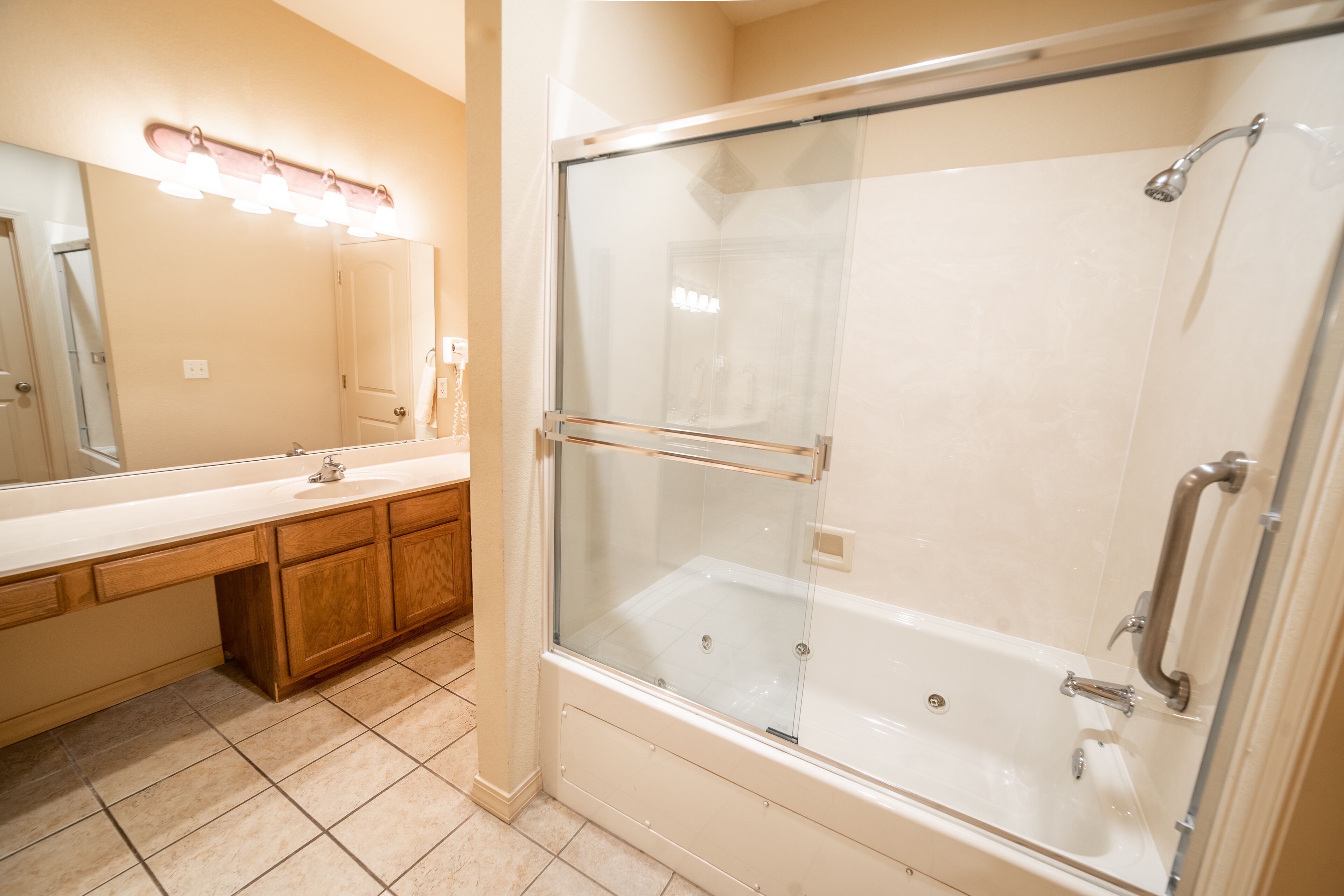 A bathroom with a glass-enclosed shower, a vanity with a mirror and lights, and wooden cabinets.