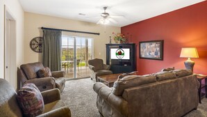A living room with a ceiling fan, a fireplace, and a large window. - 2 King Suites • Golf Course Condo • Minutes to Branson Shows & Attractions (Branson)