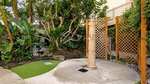 Un jardín con un sendero de concreto, una pequeña sección de césped artificial y una valla de madera celosía.