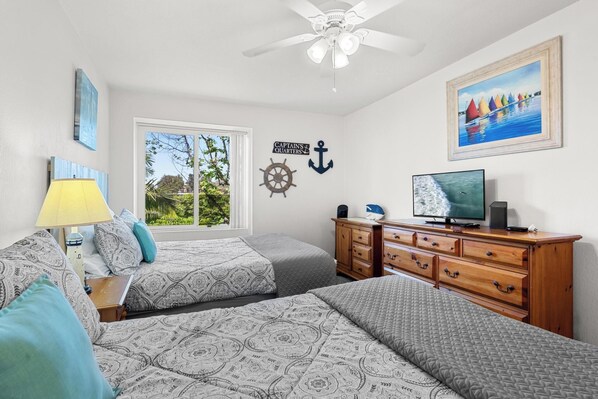 Un dormitorio con dos camas, televisor, cómoda, ventilador de techo y decoración temática náutica.
