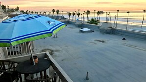 A rooftop terrace with a view of the beach, palm trees, and a pier.