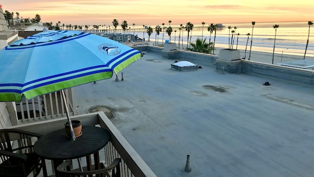 Een dakterras met uitzicht op het strand, palmbomen en een pier.