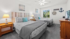 A bedroom with two beds, a ceiling fan, and nautical-themed decor.