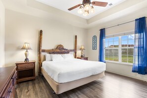 A bedroom with a large bed, wooden headboard, two bedside tables with lamps, a ceiling fan, and a window with blue curtains. - Spacious 2-Bedroom Golf Condo in hte Heart of Branson (Branson)