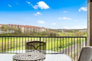 A balcony with a table and chairs, overlooking a golf course and a large building complex. - Spacious 2-Bedroom Golf Condo in hte Heart of Branson (Branson)
