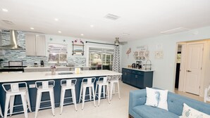 Een moderne keuken met een centraal eiland, barkrukken, een blauwe bank en een koffiebar.