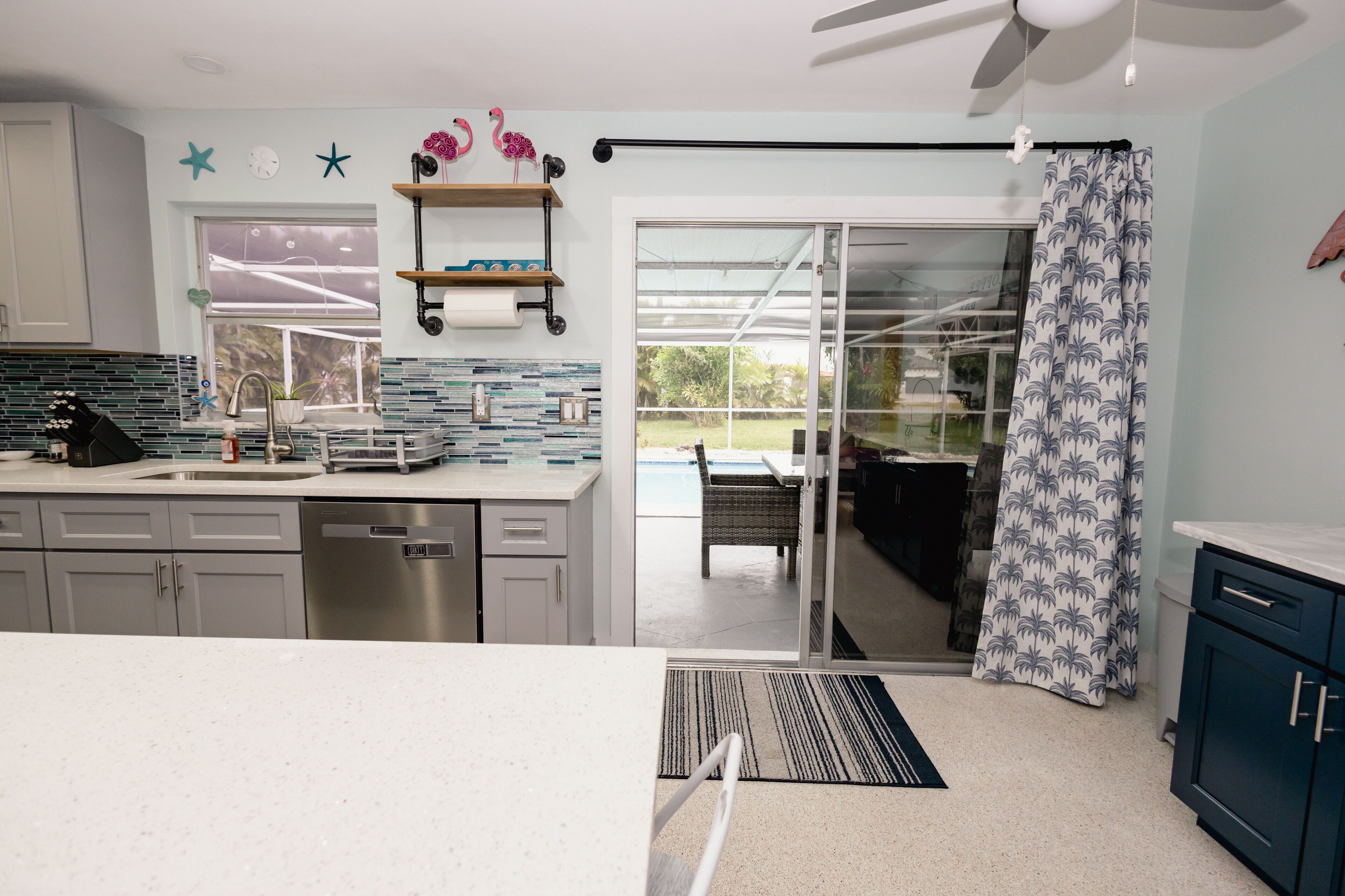 A modern kitchen with a dishwasher, a window with a view of the outdoors, and a sliding glass door leading to a patio area.