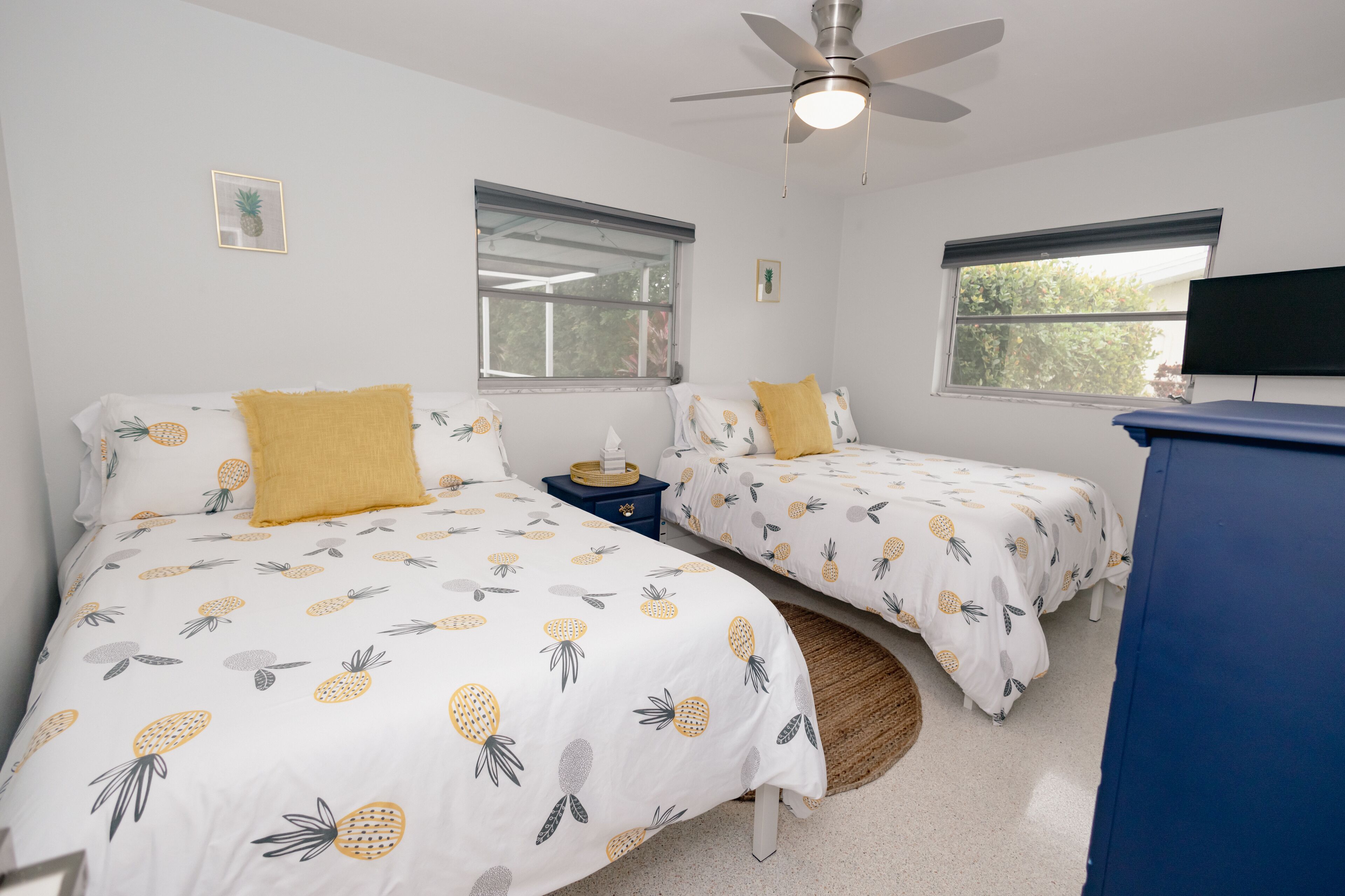 Un dormitorio con dos camas, cada una con una colcha con motivos de piña, un ventilador de techo y un televisor en la pared.